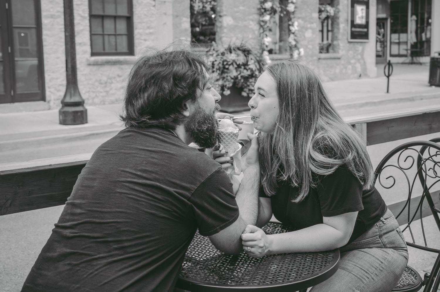 A couple shares ice cream at an outdoor cafe table in black and white.