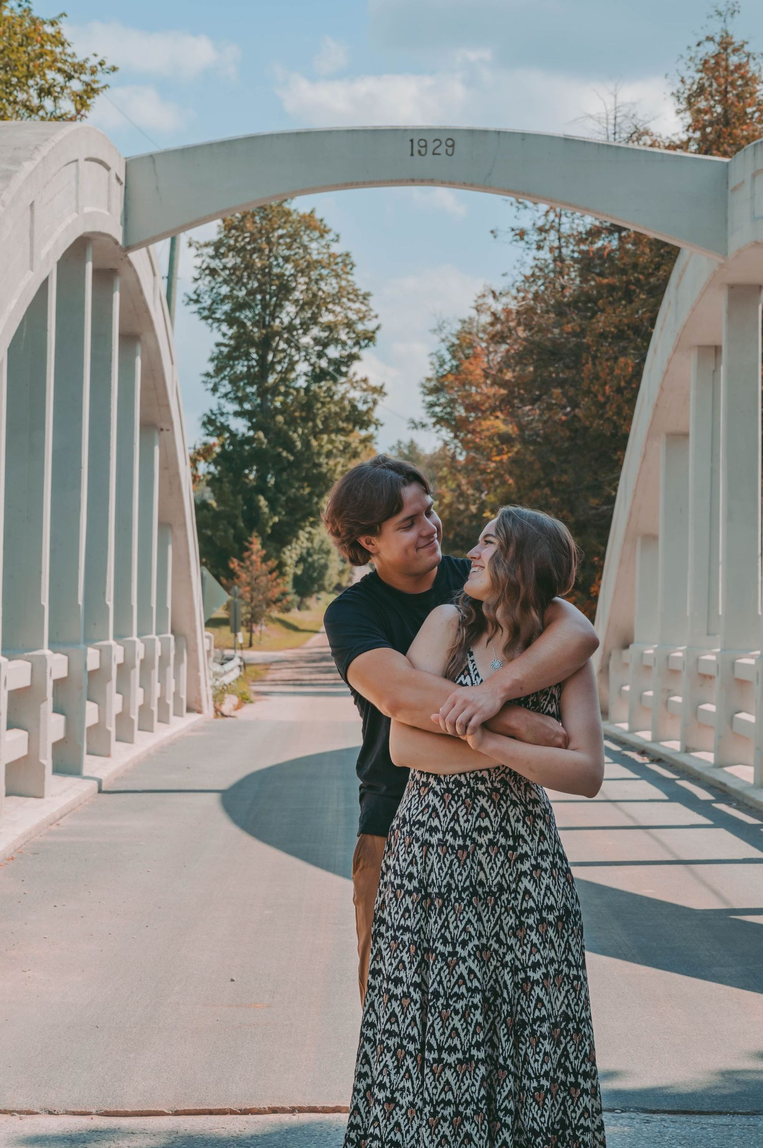 Couple embracing on historic white bridge marked 1928 during engagement photoshoot.