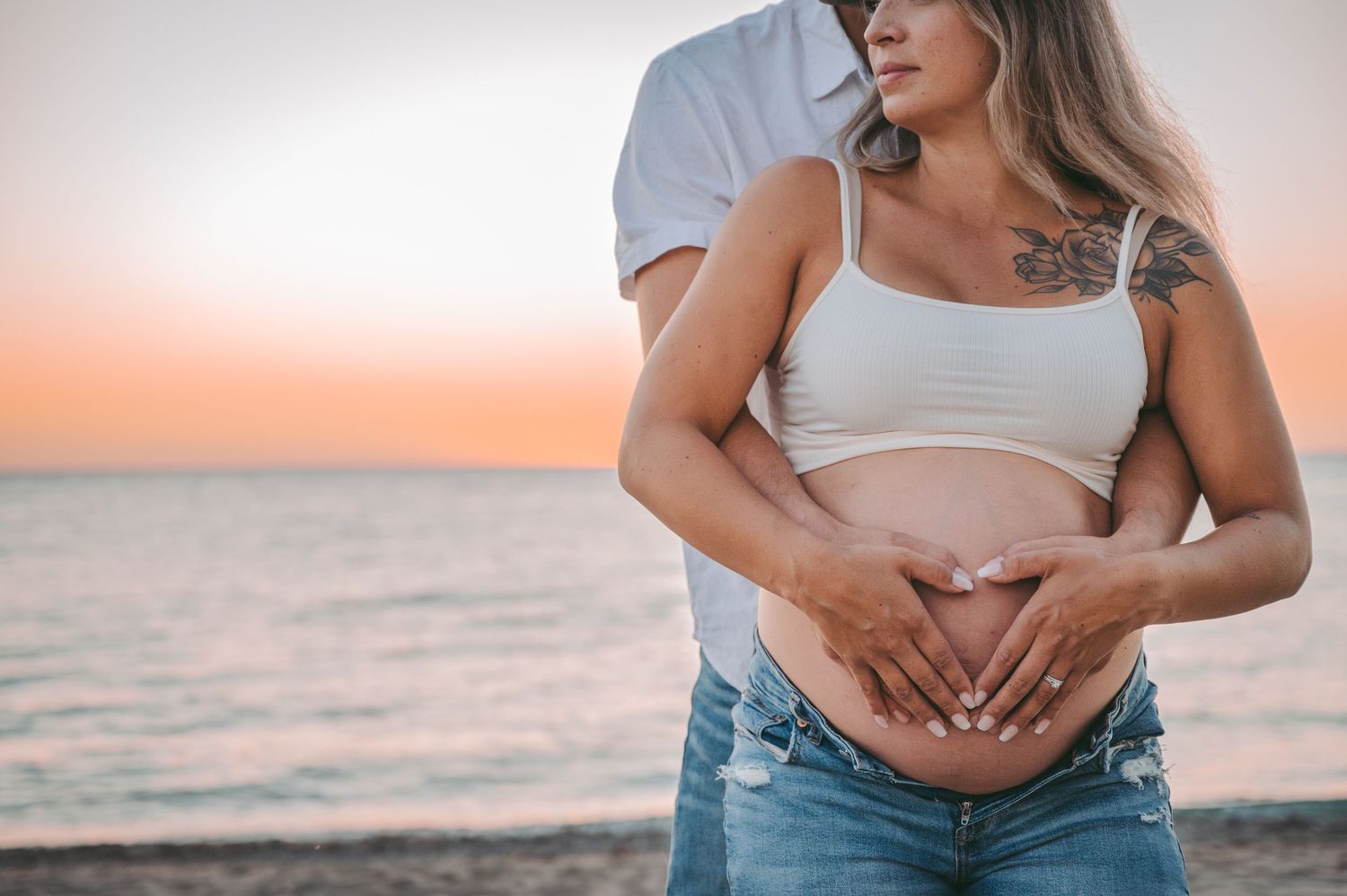 Intimate maternity photography showing baby bump at beach during golden hour sunset.