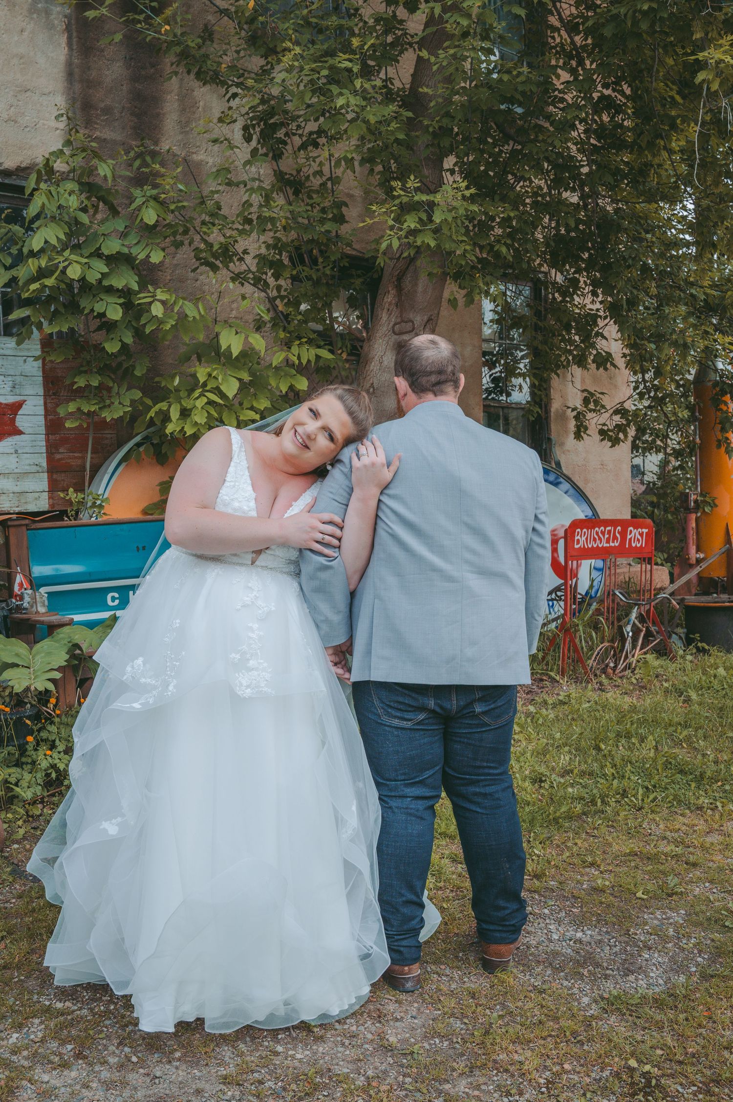 Newlyweds share an intimate moment outdoors against a backdrop of greenery and vintage decor.
