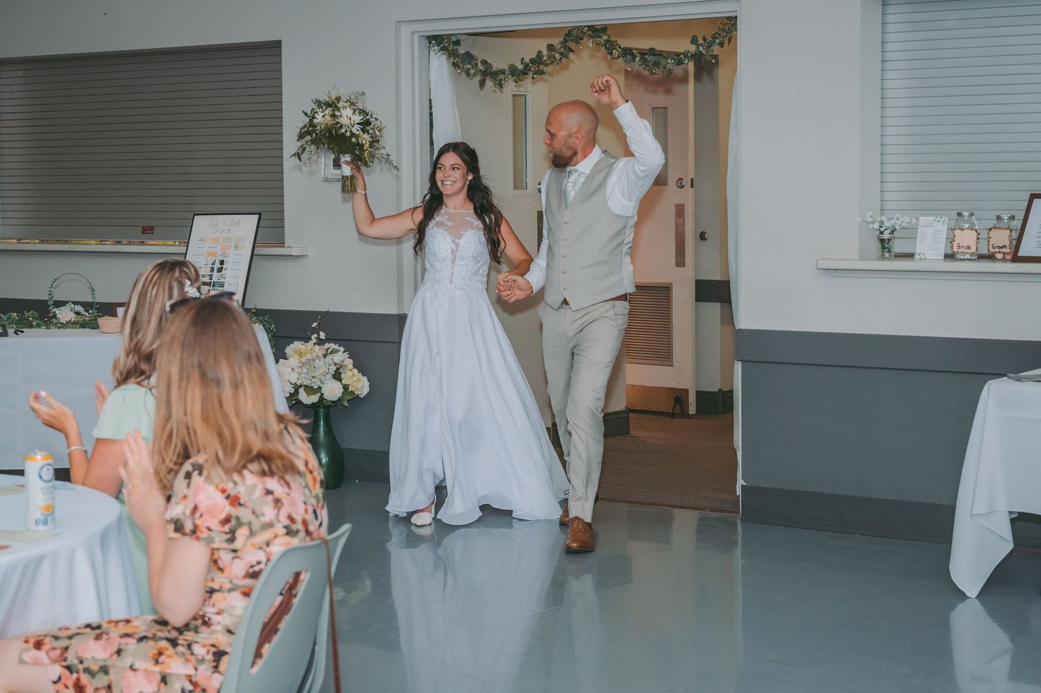 A couple makes their grand entrance into their wedding reception as guests applaud.