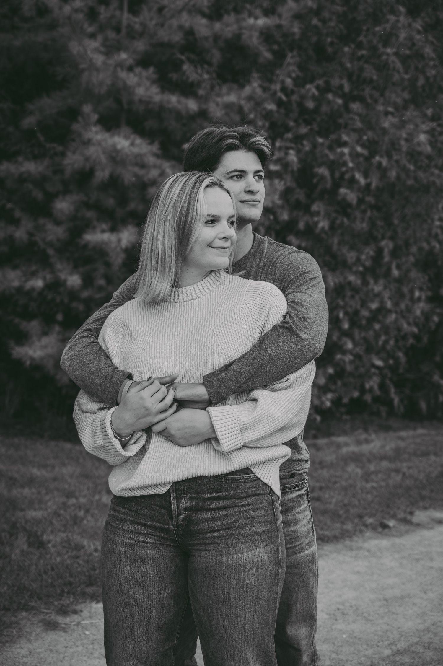 A romantic black and white portrait of a couple embracing while wearing cozy sweaters outdoors.