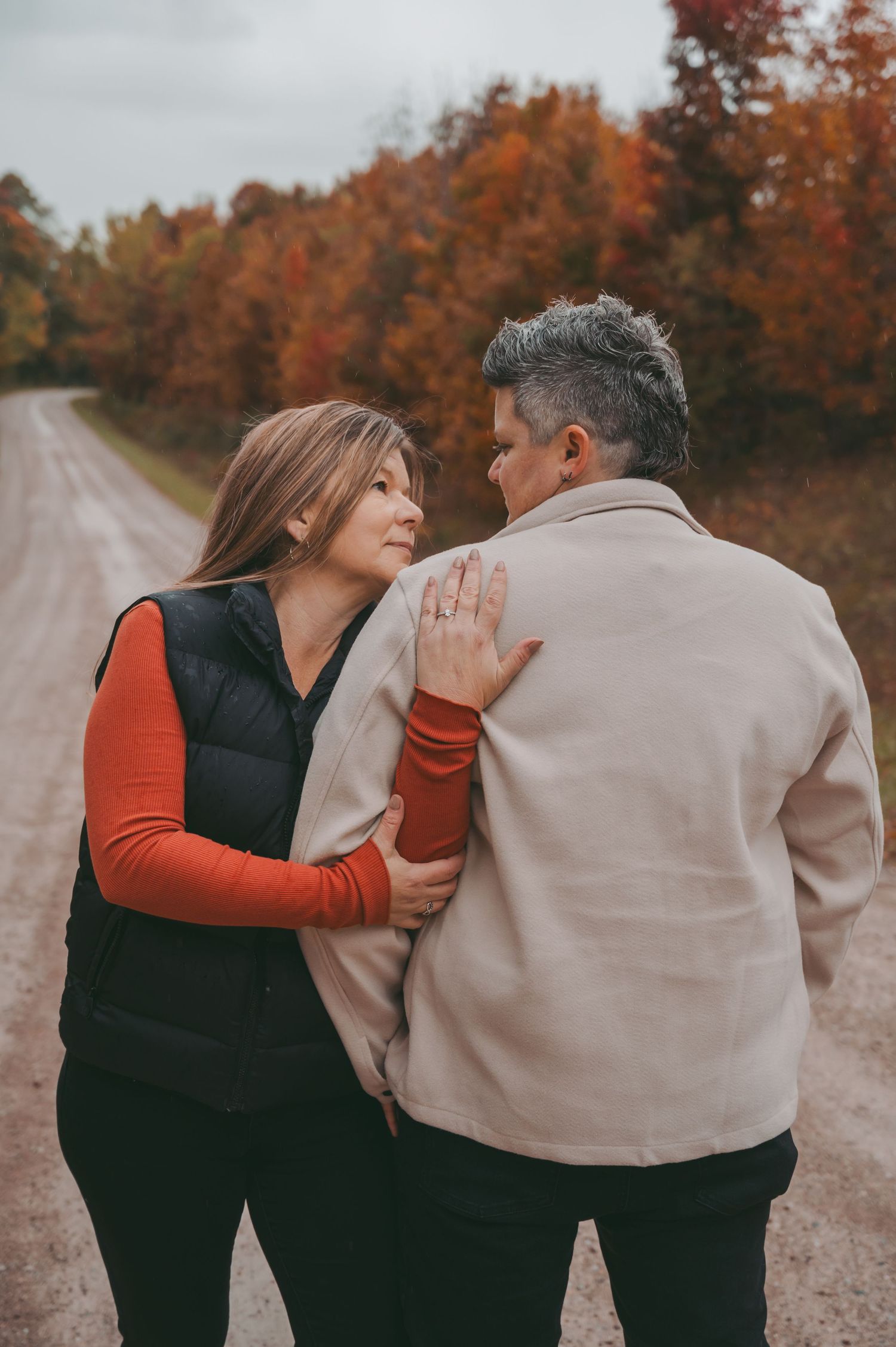 A couple sharing an intimate moment on a rural road lined with autumn trees.