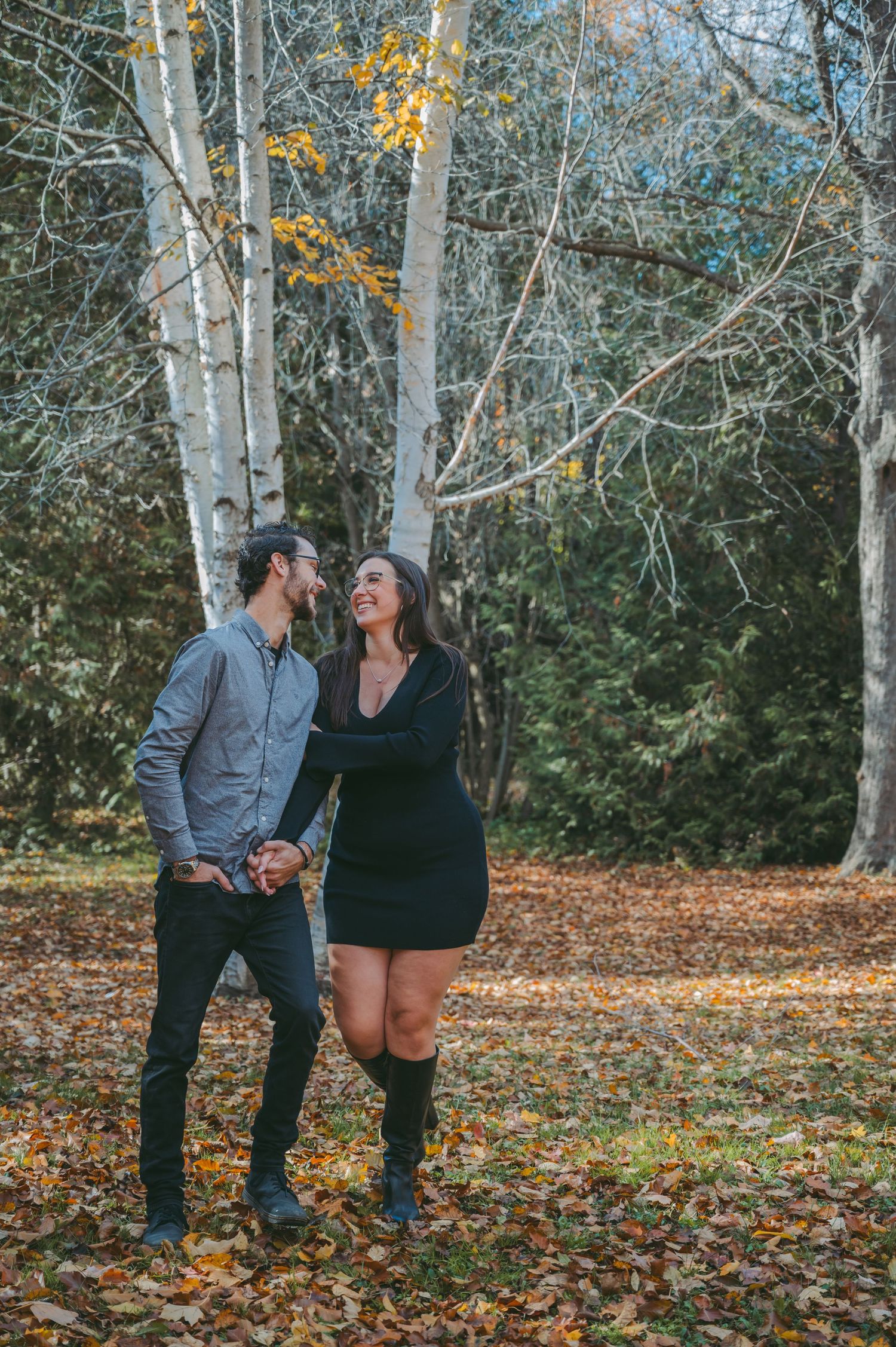 A couple shares a playful moment while walking through an autumn forest with birch trees.