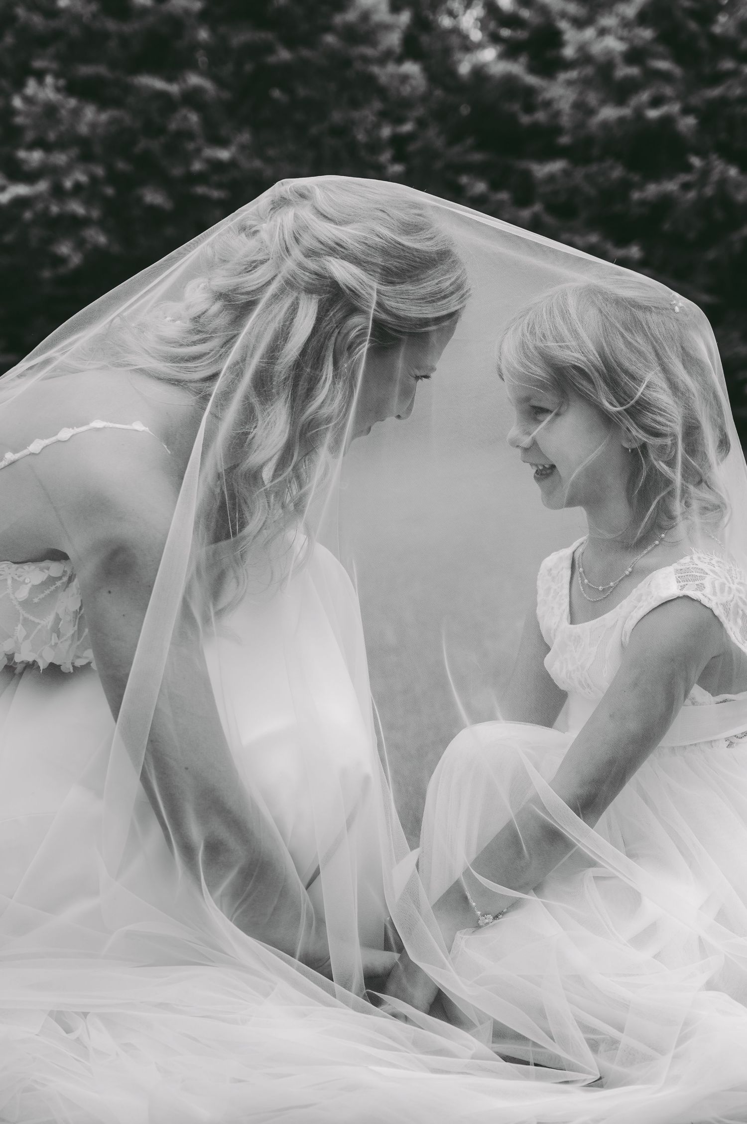 Ethereal black and white close-up shots of bride and flower girl under a flowing bridal veil in soft natural light.