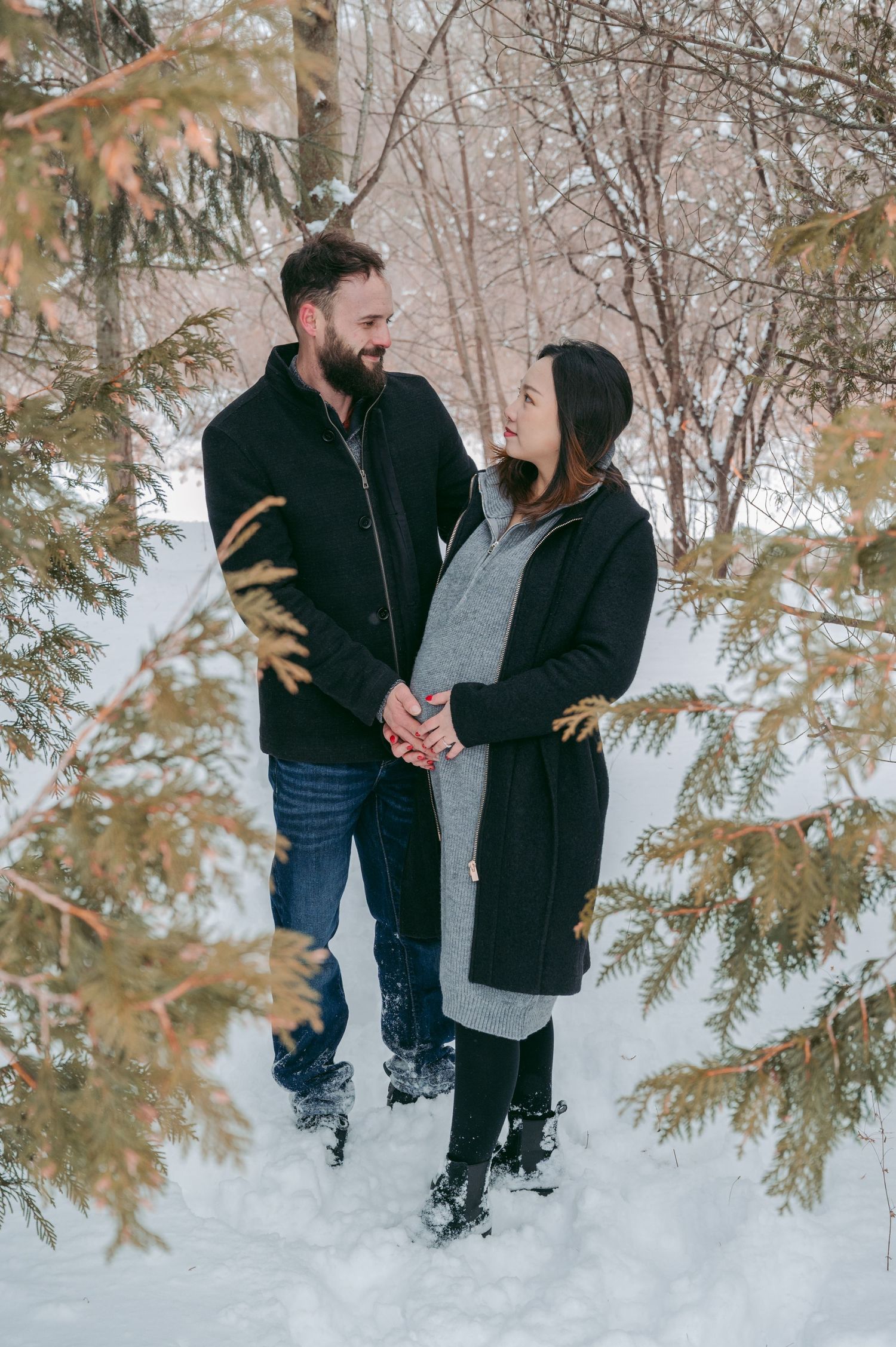 Couple sharing a moment in a snowy winter forest setting with evergreen branches.