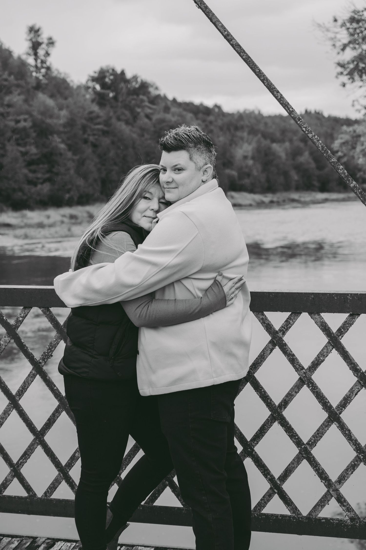 A tender embrace captured in black and white on a bridge overlooking water.
