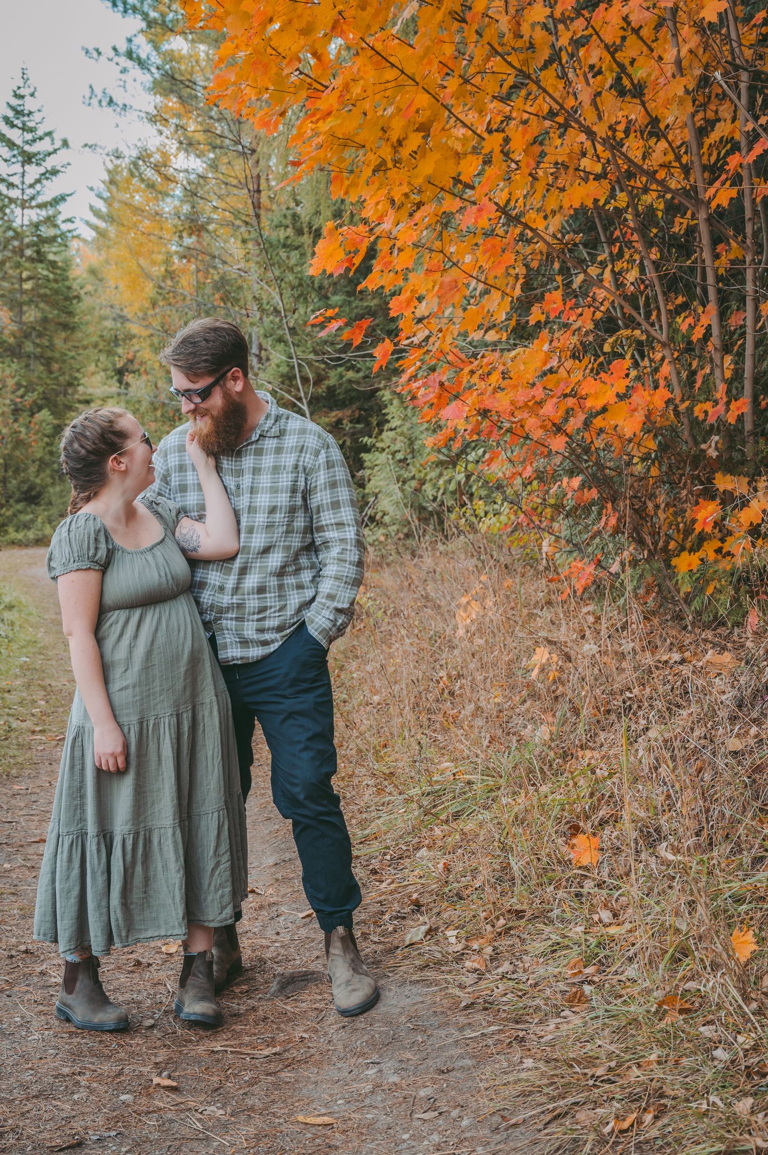A couple shares an intimate moment on a forest path with vibrant orange fall foliage.