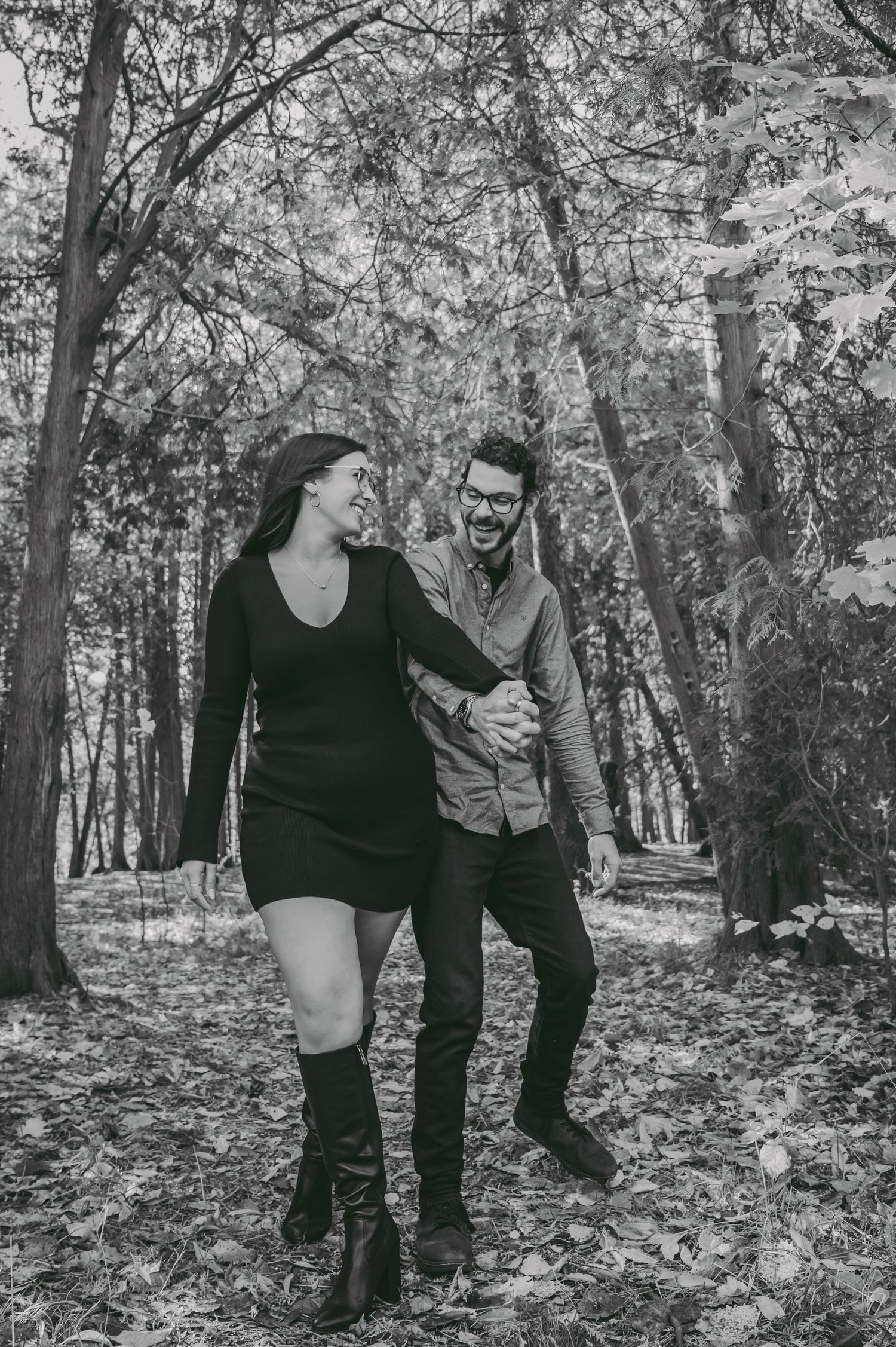 A couple laughs together while walking through a wooded path in black and white photography.