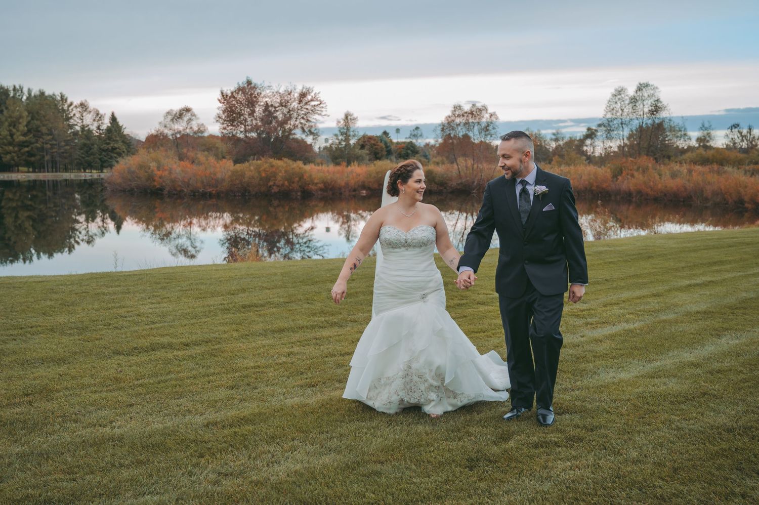 Joyful couple walking together on manicured lawn with lake and trees in background.