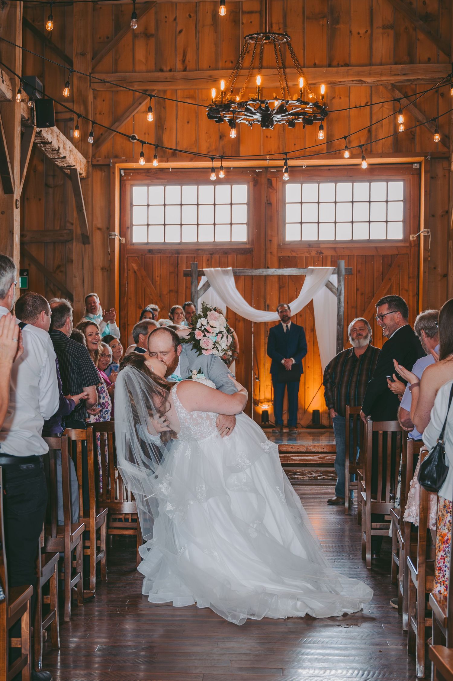 Celebratory moment in rustic barn venue with string lights during wedding ceremony.