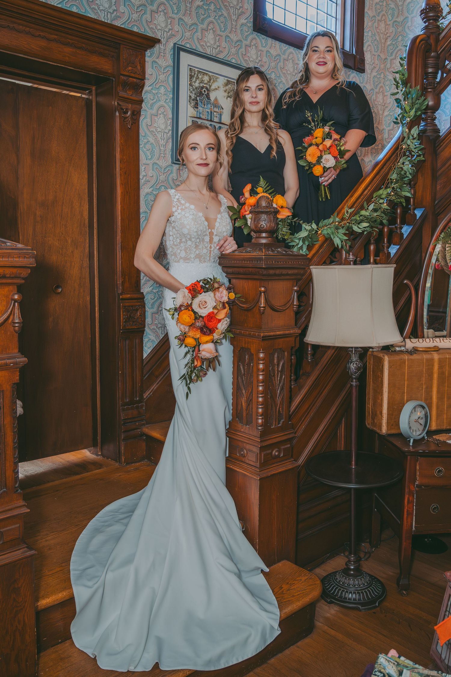 Wedding party poses on wooden staircase inside historic home with orange floral bouquets.