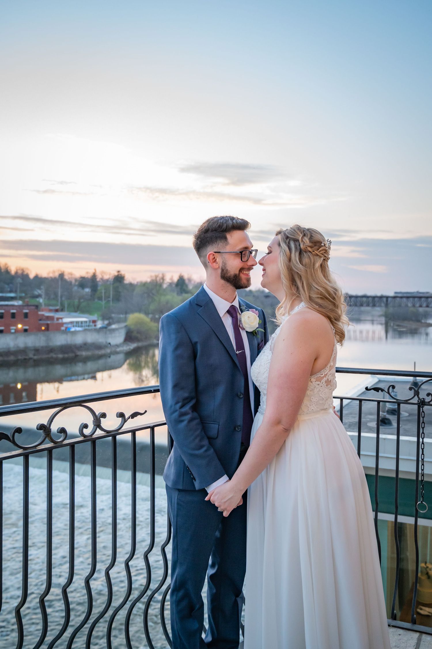 A couple shares an intimate moment on a waterfront balcony at the Cambridge Mill overlooking a marina at sunset.