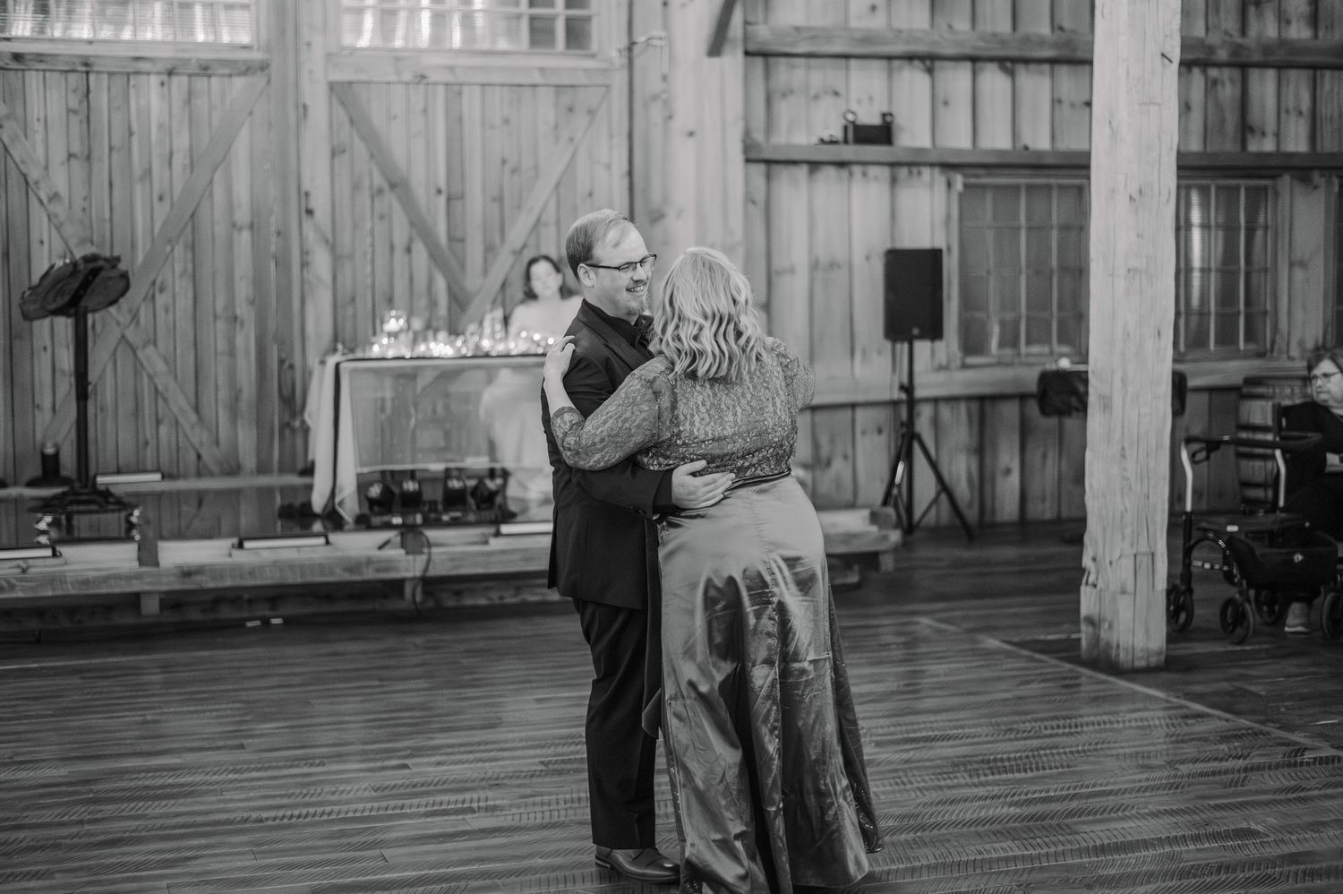 Couple shares an intimate first dance in a rustic barn wedding venue in black and white photography.