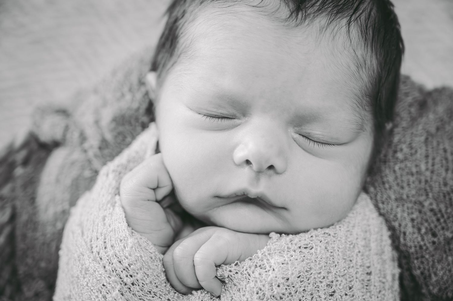 Black and white photo of sleeping newborn wrapped in knit blanket.
