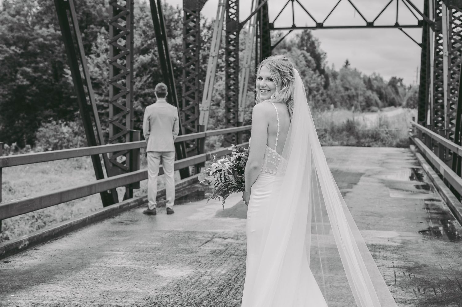 Wedding couple poses on rustic iron bridge surrounded by natural forest scenery.