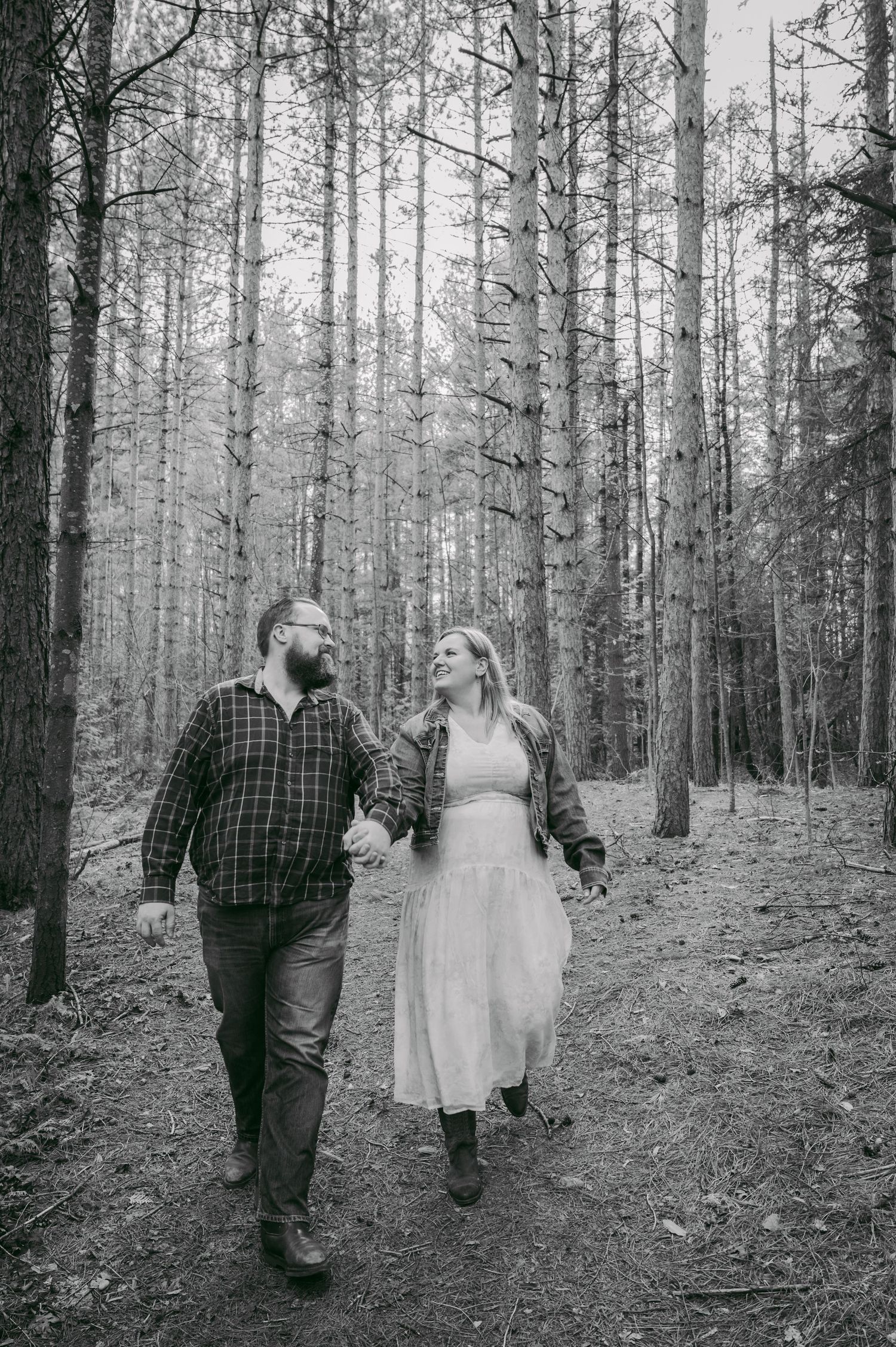 A couple strolls together through a serene forest path while wearing casual attire.