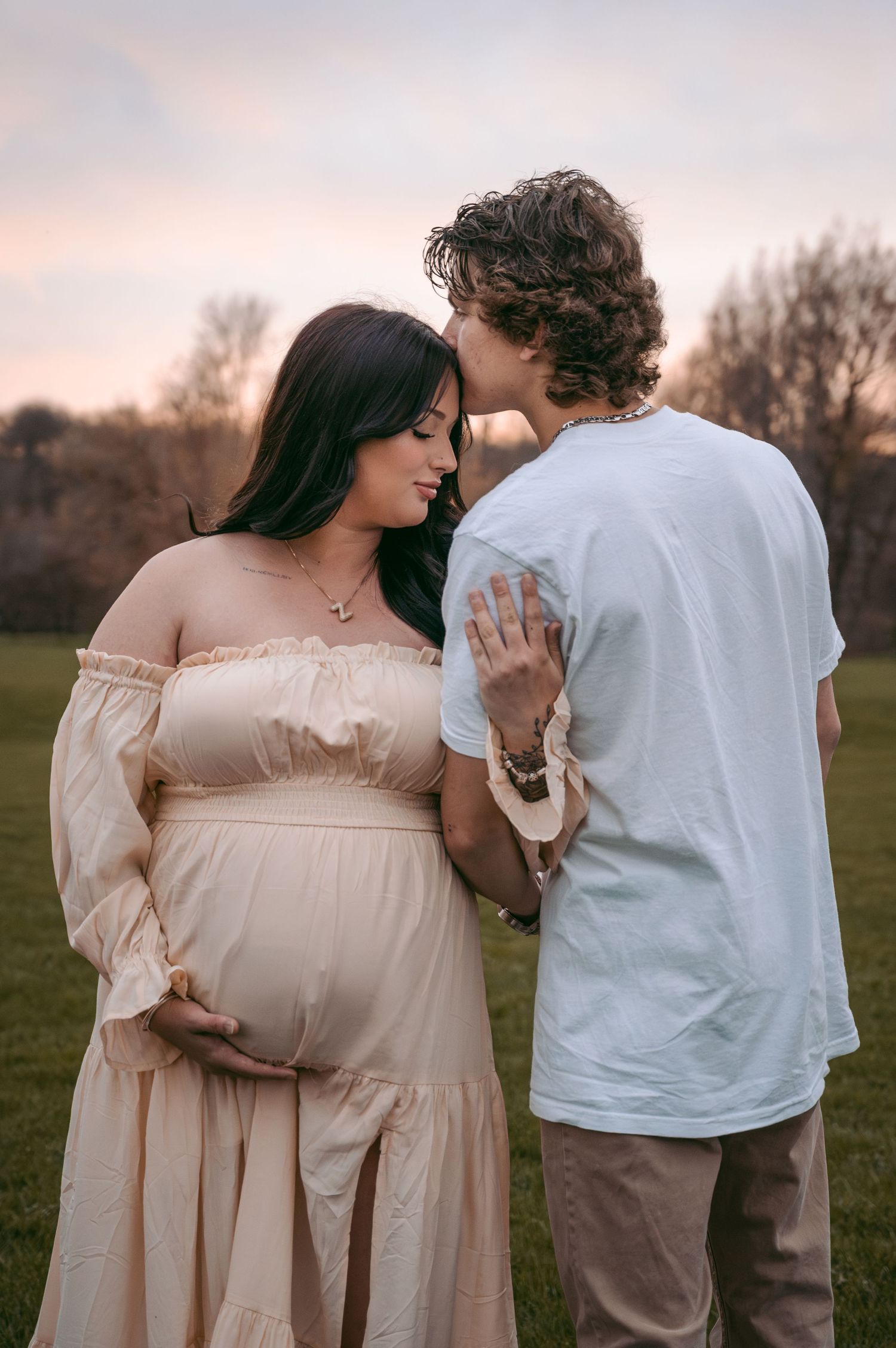 Expectant couple sharing an intimate moment during sunset maternity photoshoot in a grassy field.