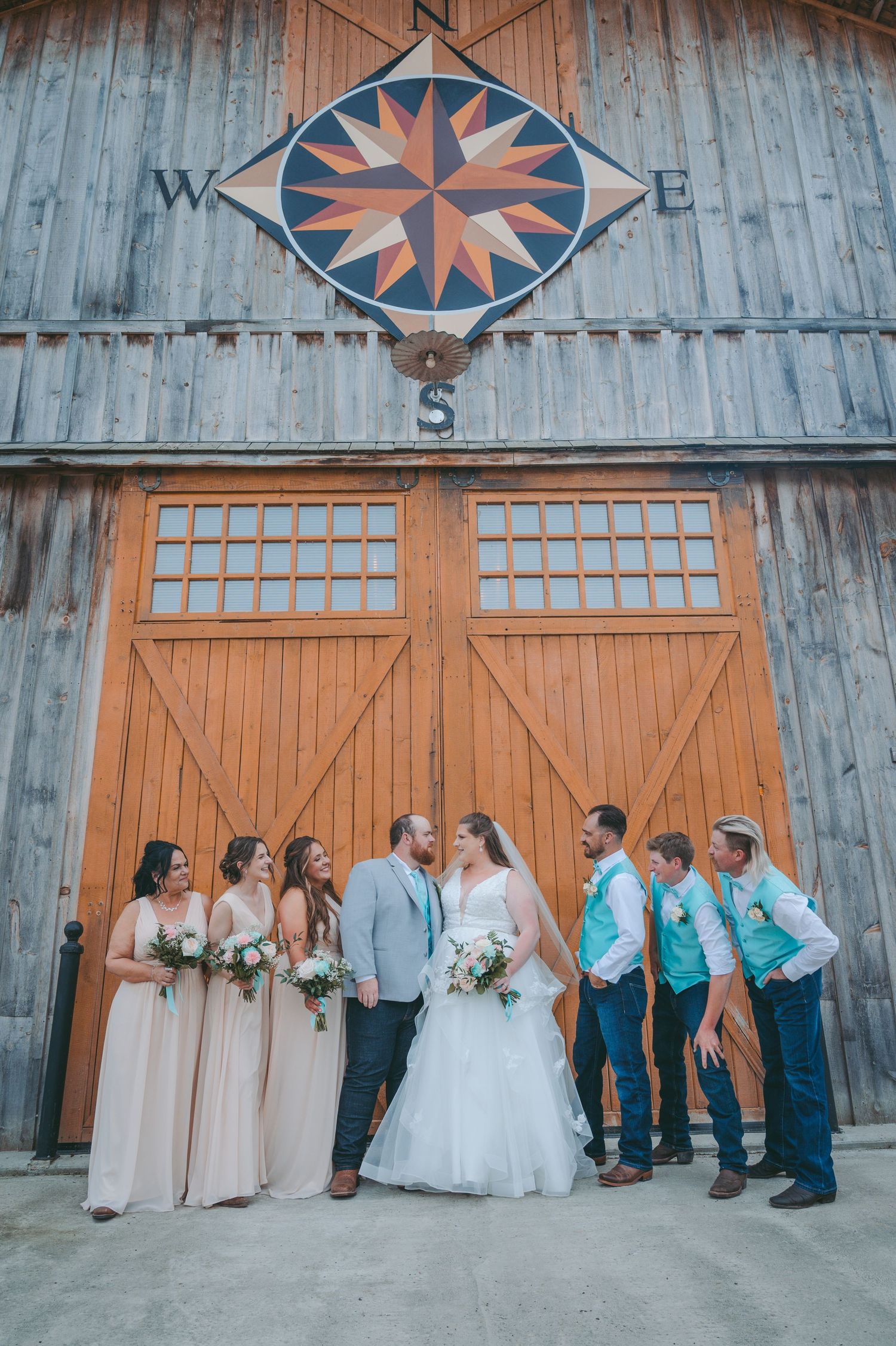 Wedding party poses under a rustic compass design on a barn exterior.