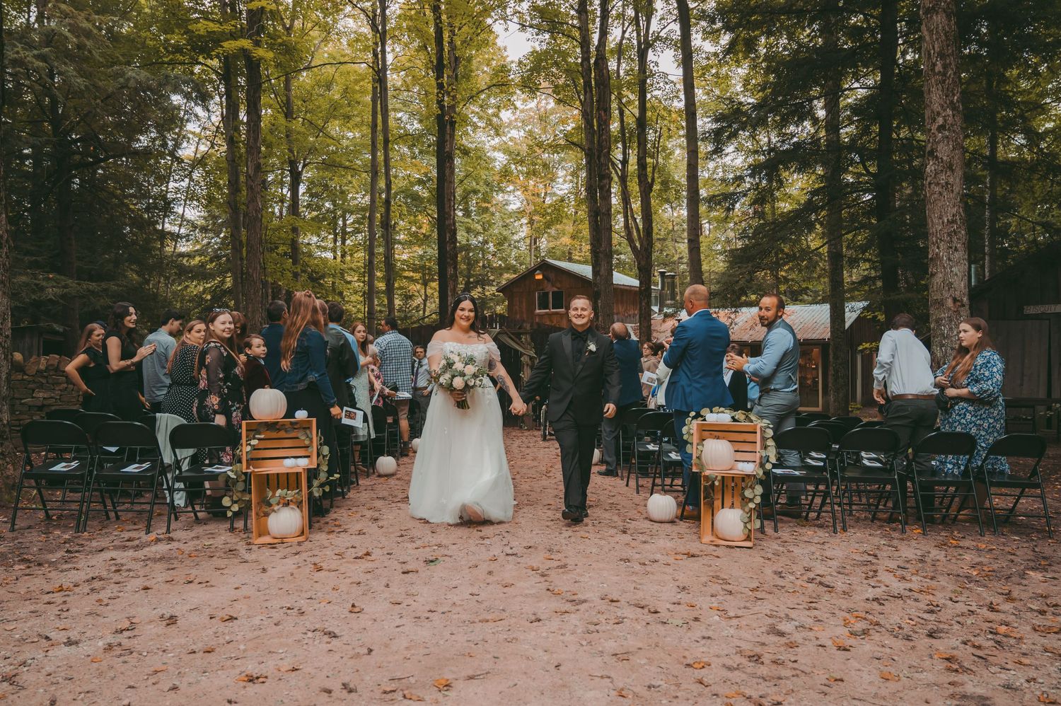 Guests seated in wooden chairs at an outdoor forest wedding ceremony at Love's Sweetness with warm autumn lighting.