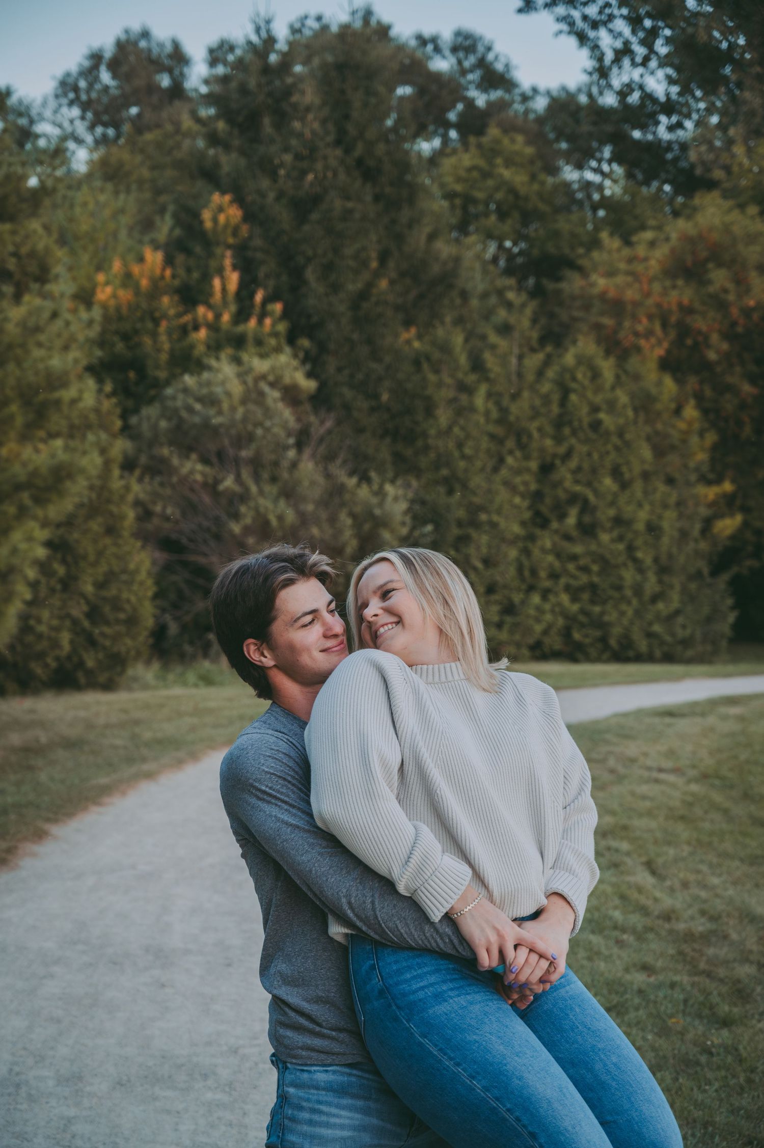 A joyful couple sharing a playful moment on a path surrounded by autumn trees.