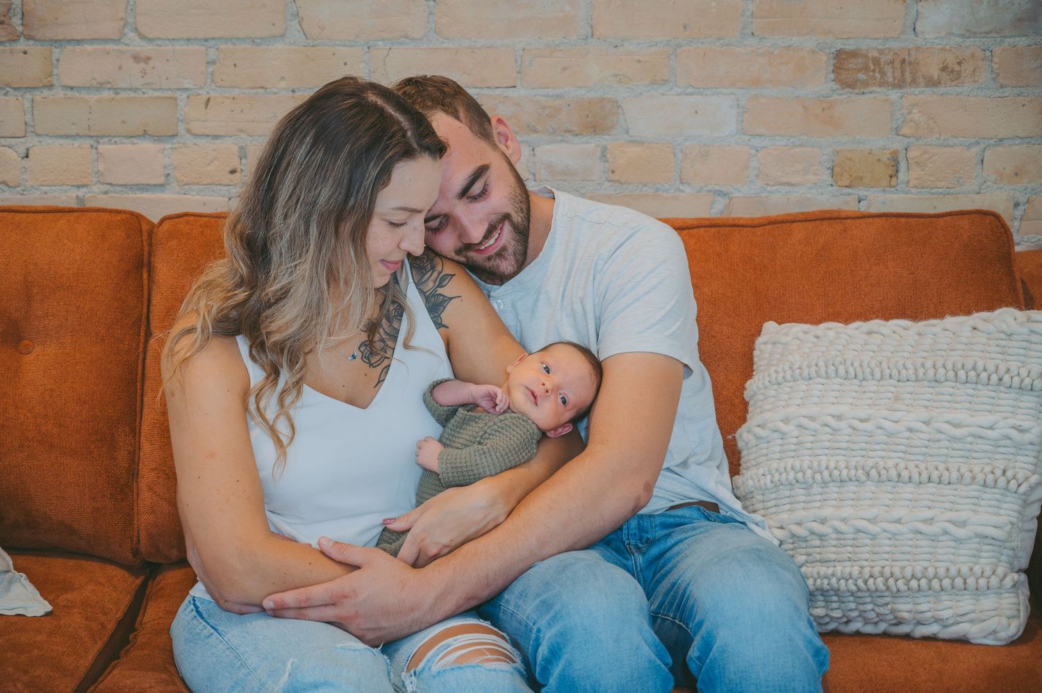 New parents cuddle with their newborn baby on an orange couch.