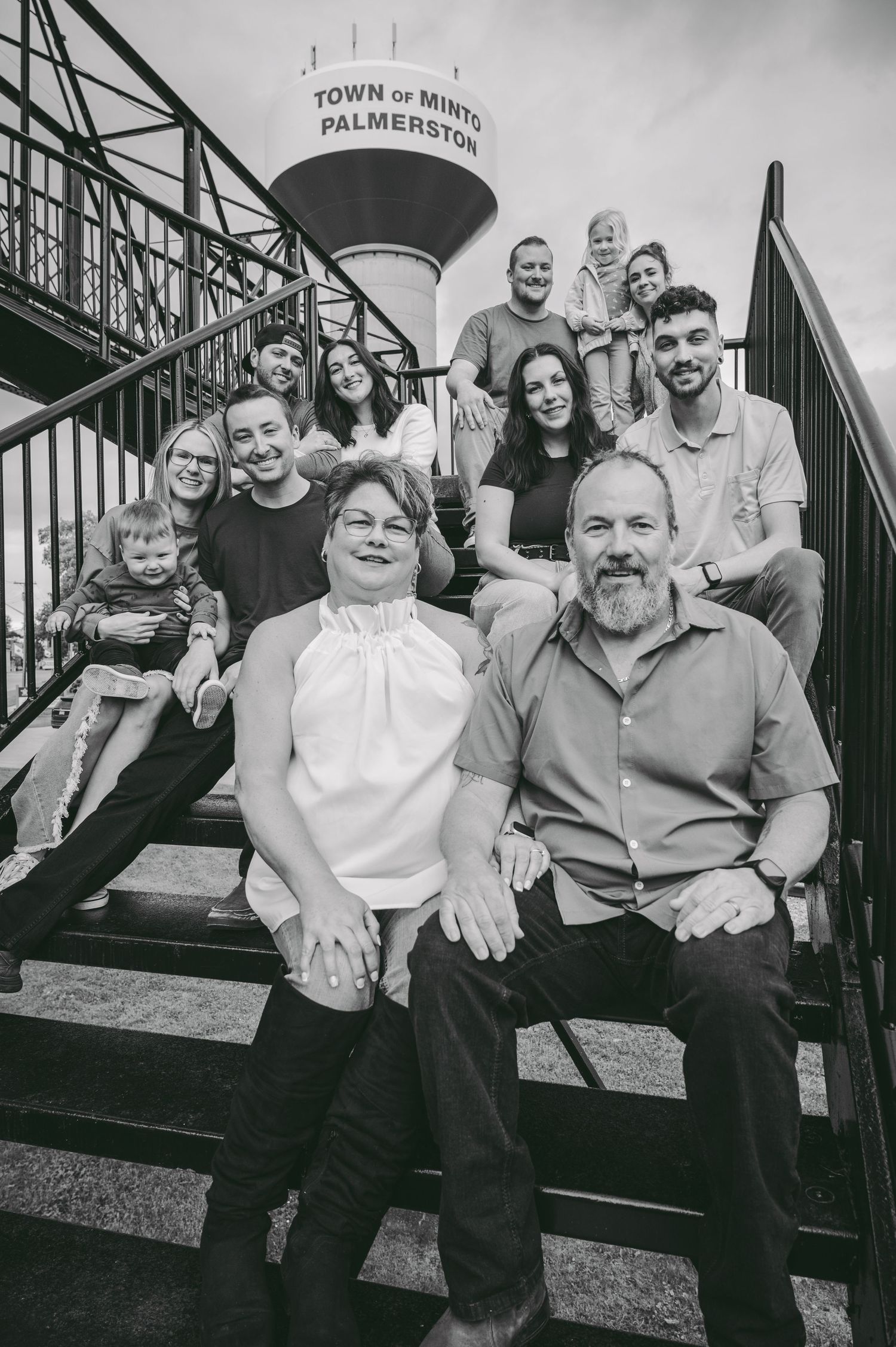 Multi-generational family portrait on outdoor stairs with water tower in background.