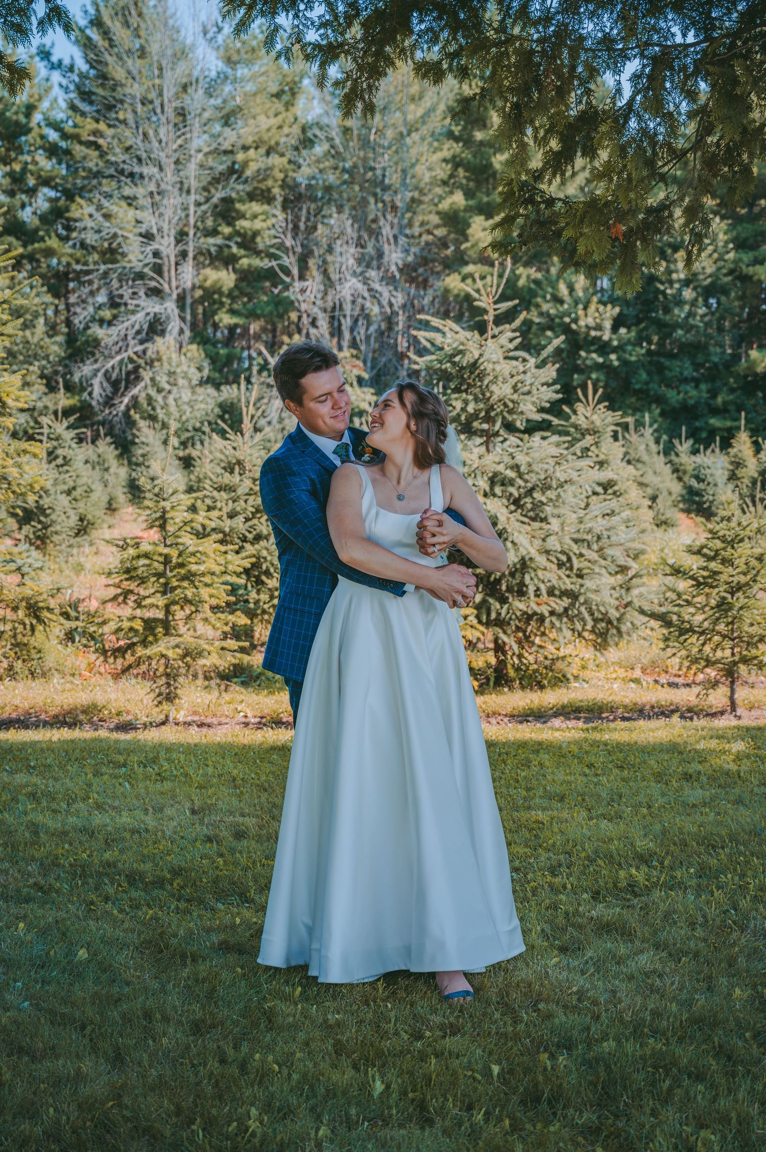 Wedding couple embracing outdoors with evergreen forest backdrop.