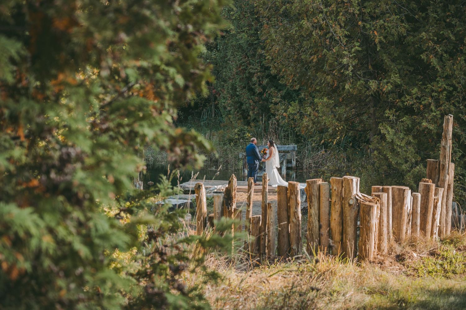 Distant view of couple among rustic wooden posts in natural outdoor setting.