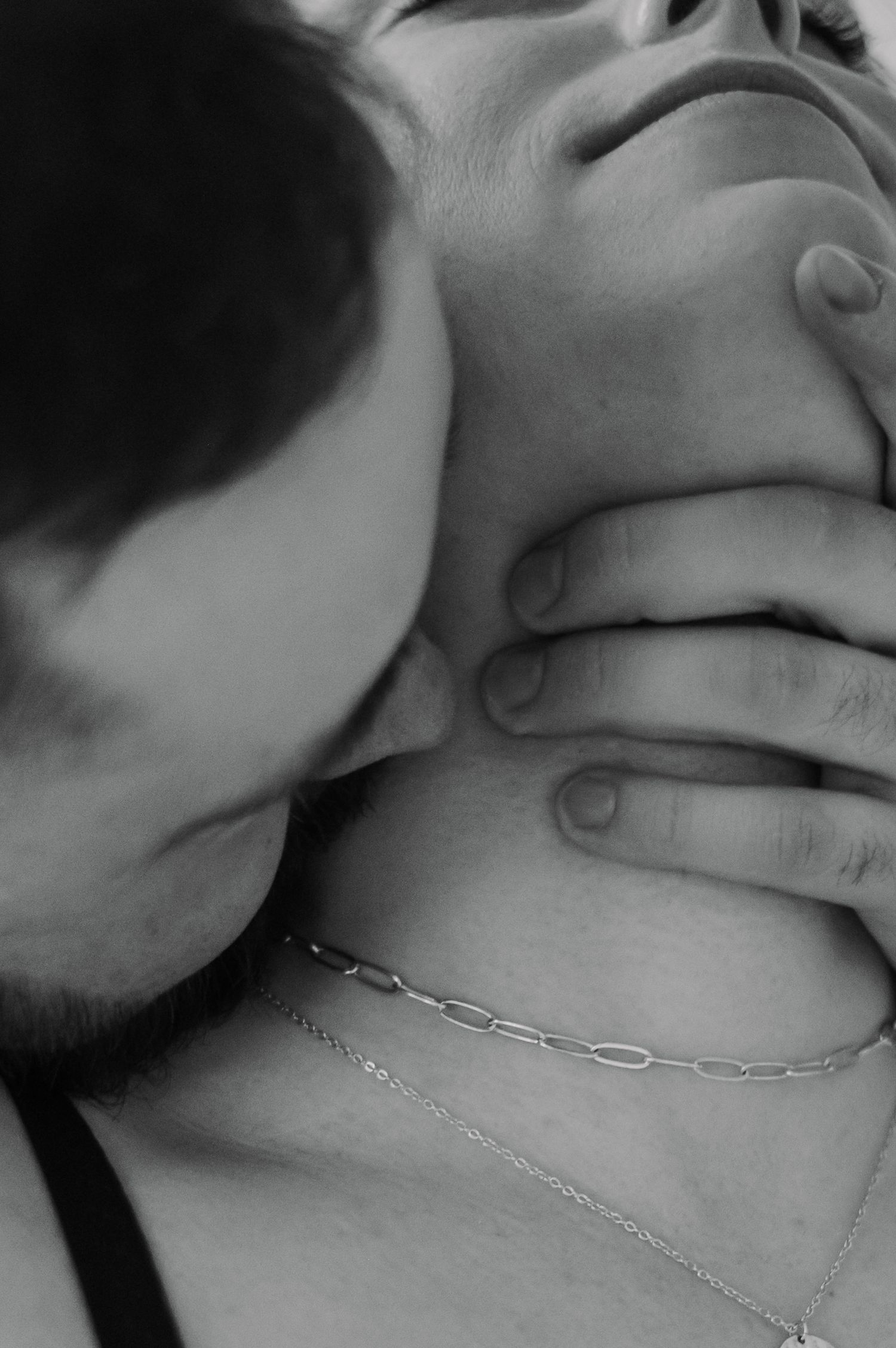 Black and white close-up of a couple in an intimate moment, man kissing womans neck while hands intertwine.