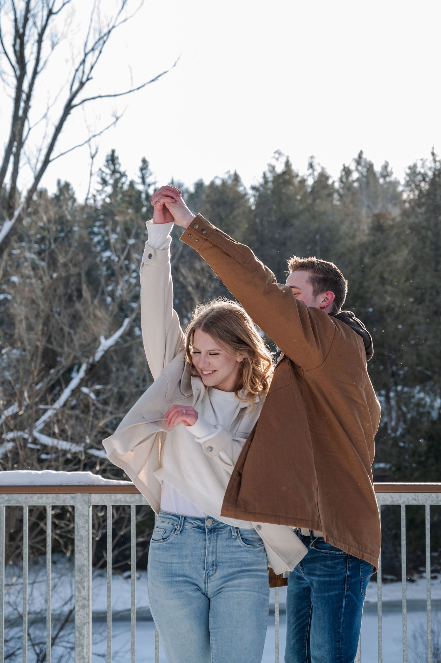 A couple in winter clothing strikes playful poses in a series of snowy outdoor photos.