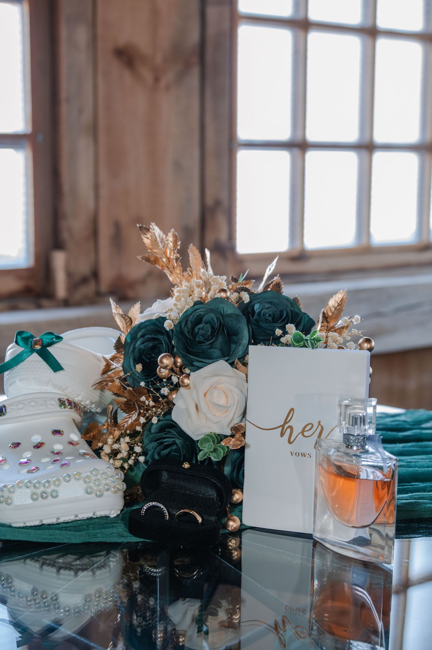Elegant wedding flat lay with teal roses bouquet, perfume bottle, rings, and a 'her' vows card on glass table.