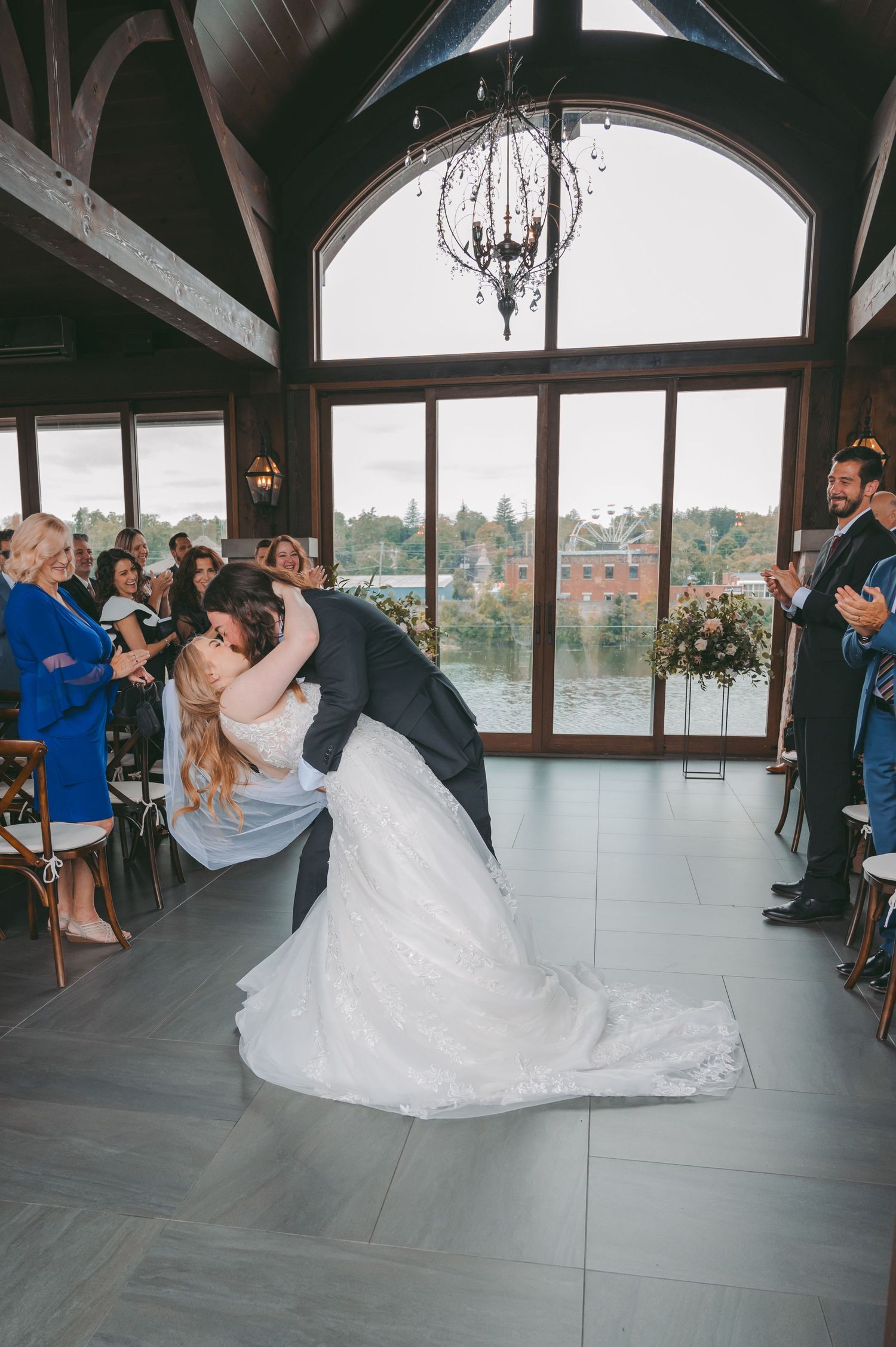 Romantic wedding dip pose in front of large windows overlooking scenic water view.