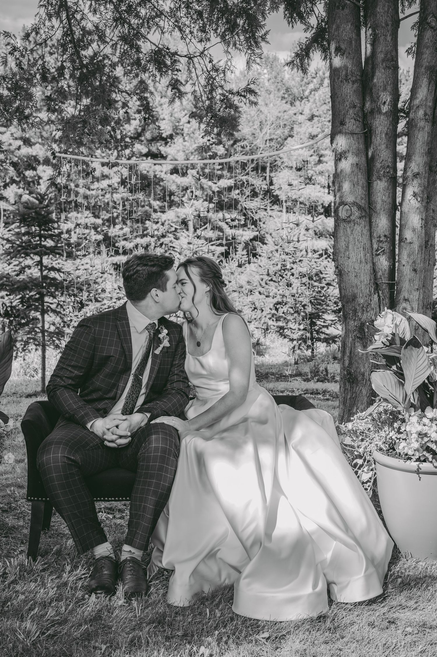 Black and white portrait of newlyweds sharing an intimate moment on a bench in a wooded setting.
