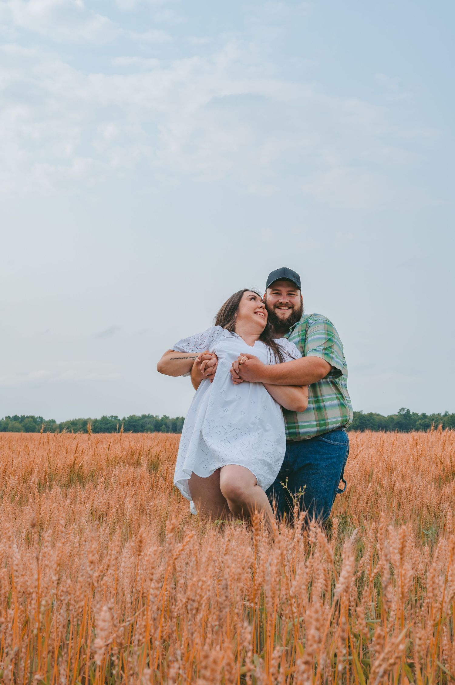 A playful couple sharing a joyful moment while dancing in a rustic wheat field.