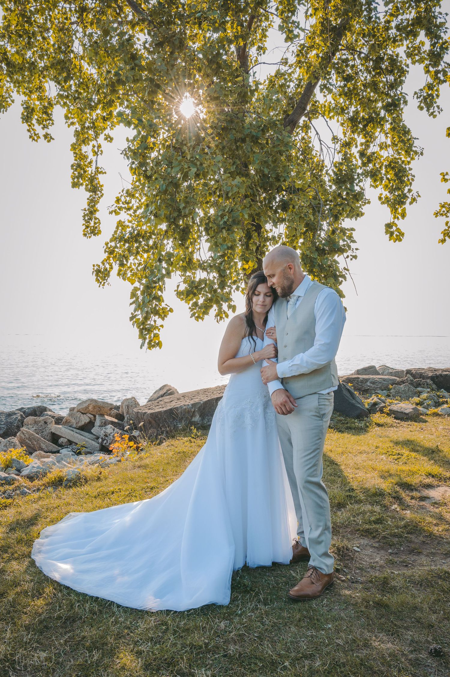 Romantic wedding photos captured by the water during golden hour with overhanging tree branches.