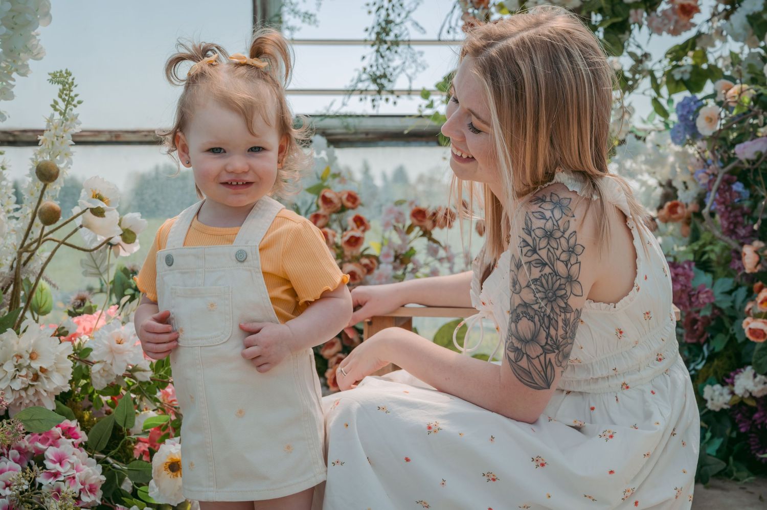 Child and mother surrounded by flowers in a greenhouse.