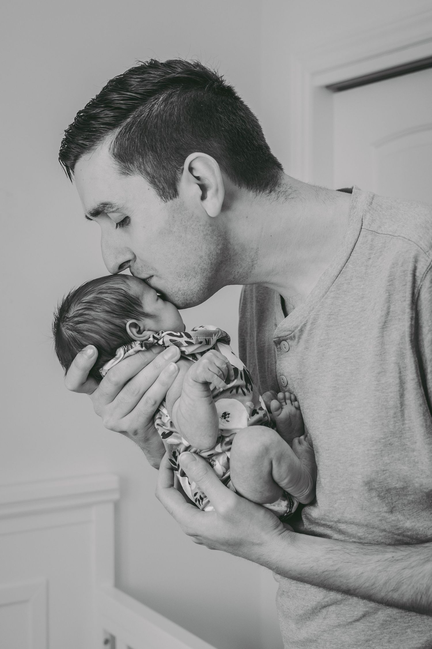 Intimate black and white moment of parent kissing newborn baby.