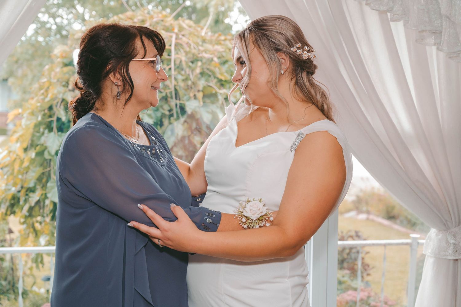 Emotional wedding moment captured between two people under white drapery outdoors.