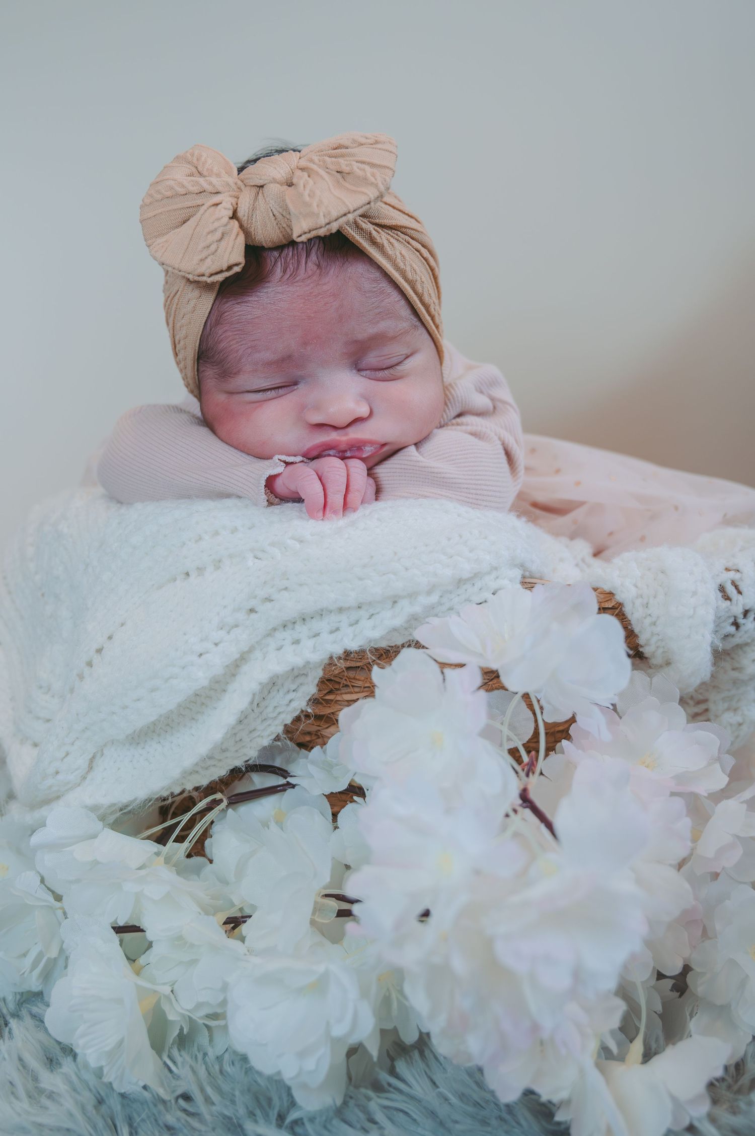 A sleeping newborn adorned with a bow lies peacefully on white lace with floral accents.