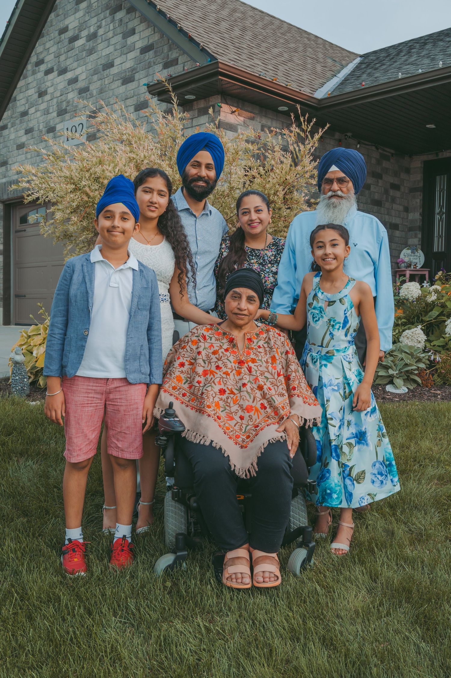 Family members sitting together on grass in coordinated outfits outside their home.