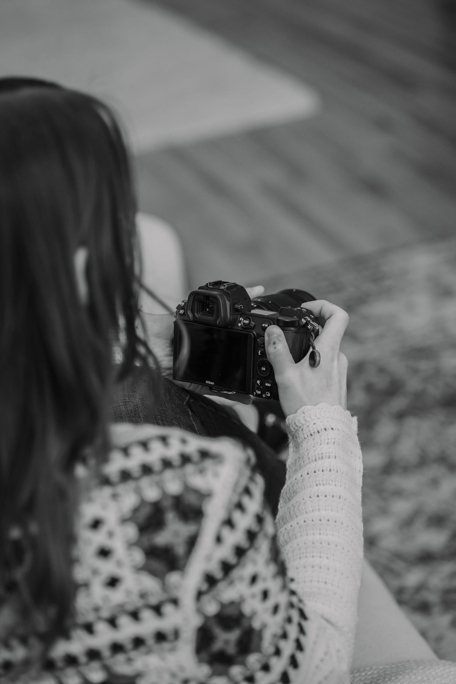 A photographer in a knit sweater holds a vintage camera in black and white.