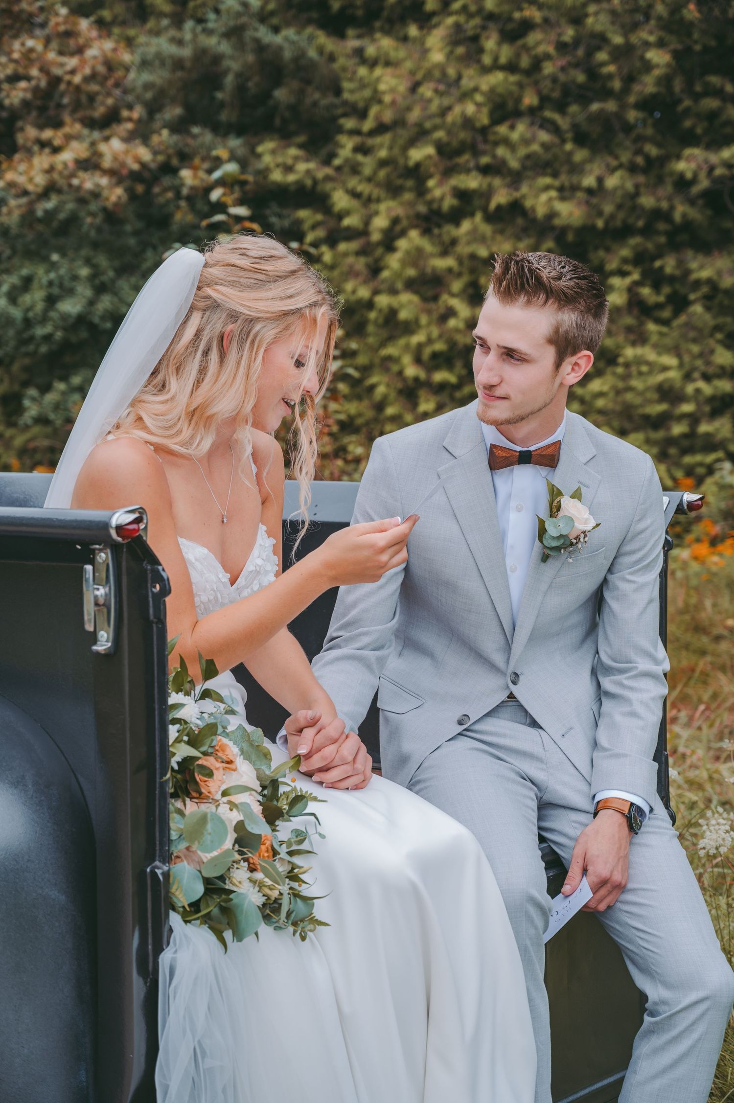 A couple in wedding attire share a candid moment while sitting together in a vintage car.