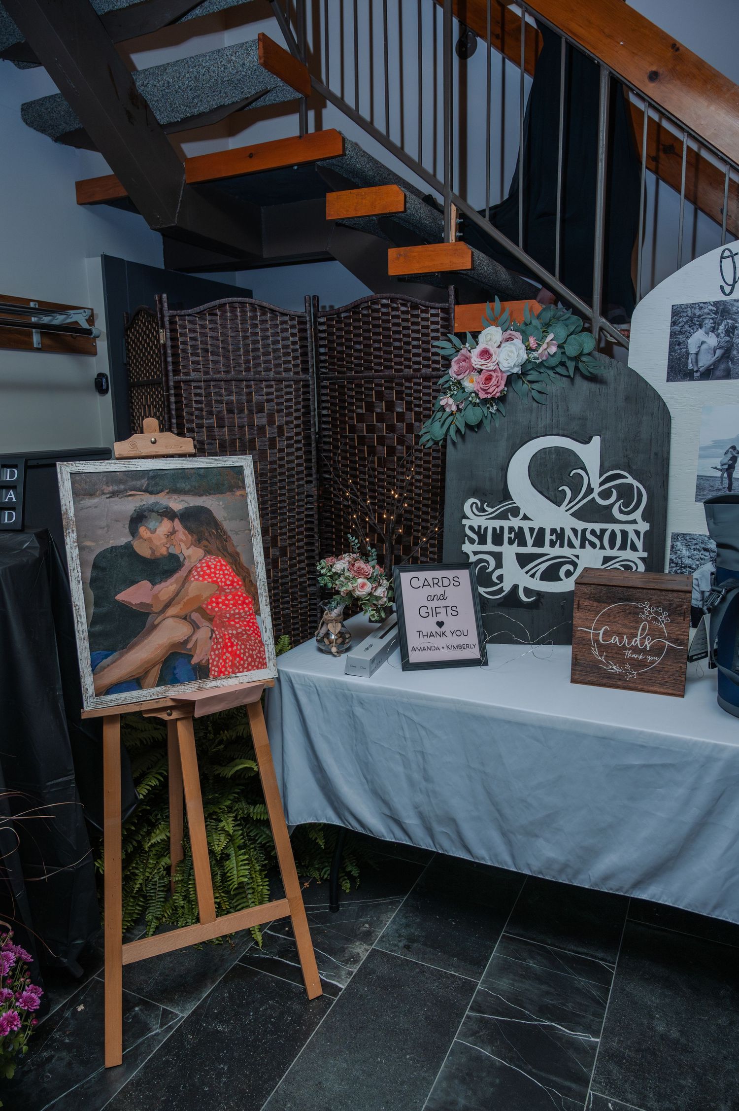 Wedding reception decor features elegant photo displays on wooden easels with floral arrangements and welcome signs.