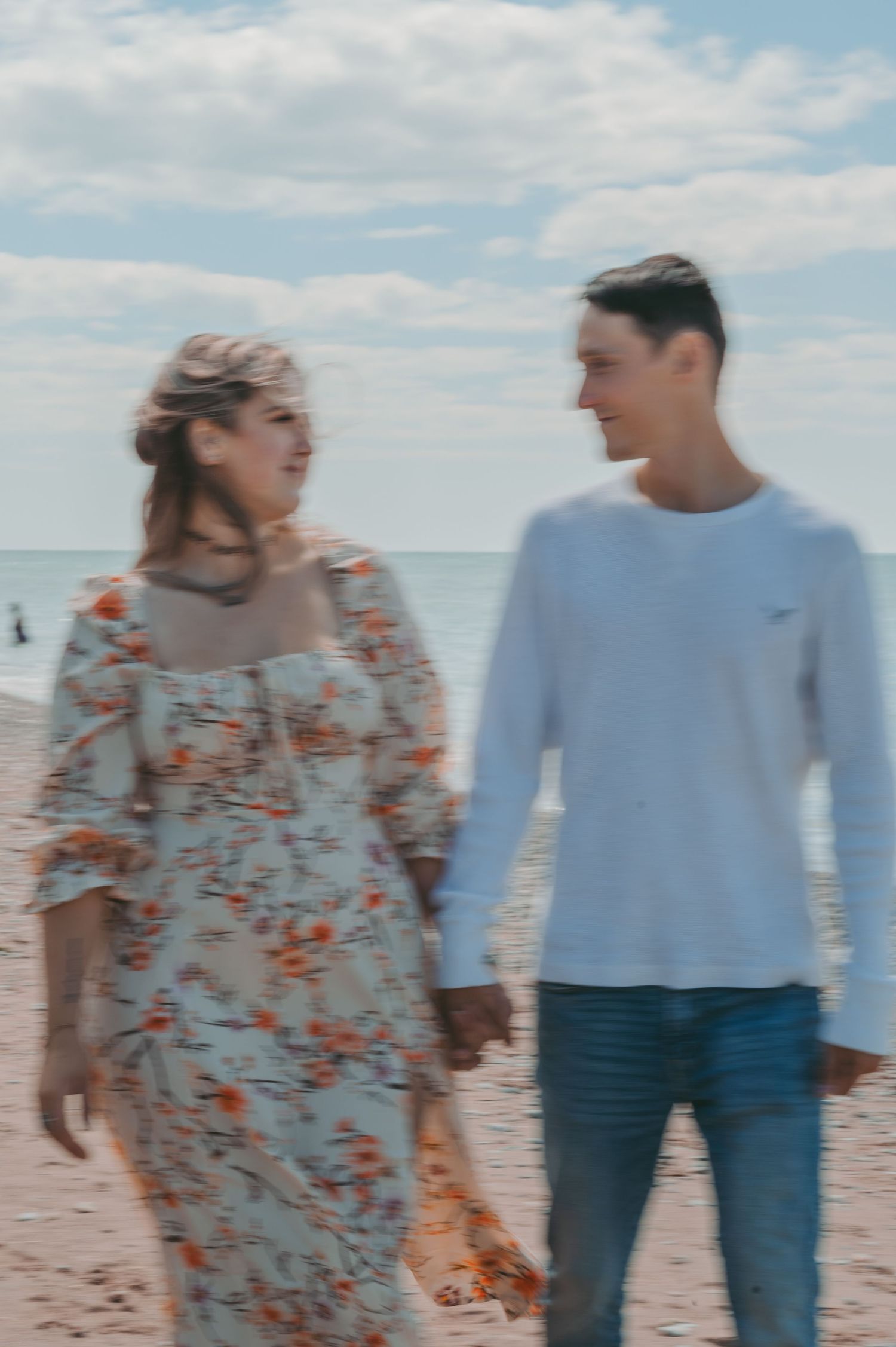 Casual beach stroll captured in soft focus with ocean and clouds in background.