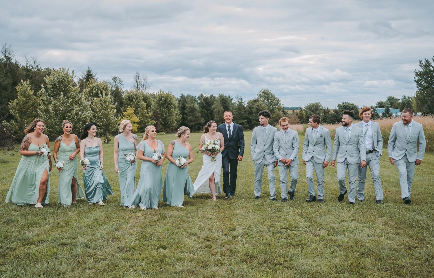 Wedding party in mint green and light gray attire lined up for a group photo outdoors.