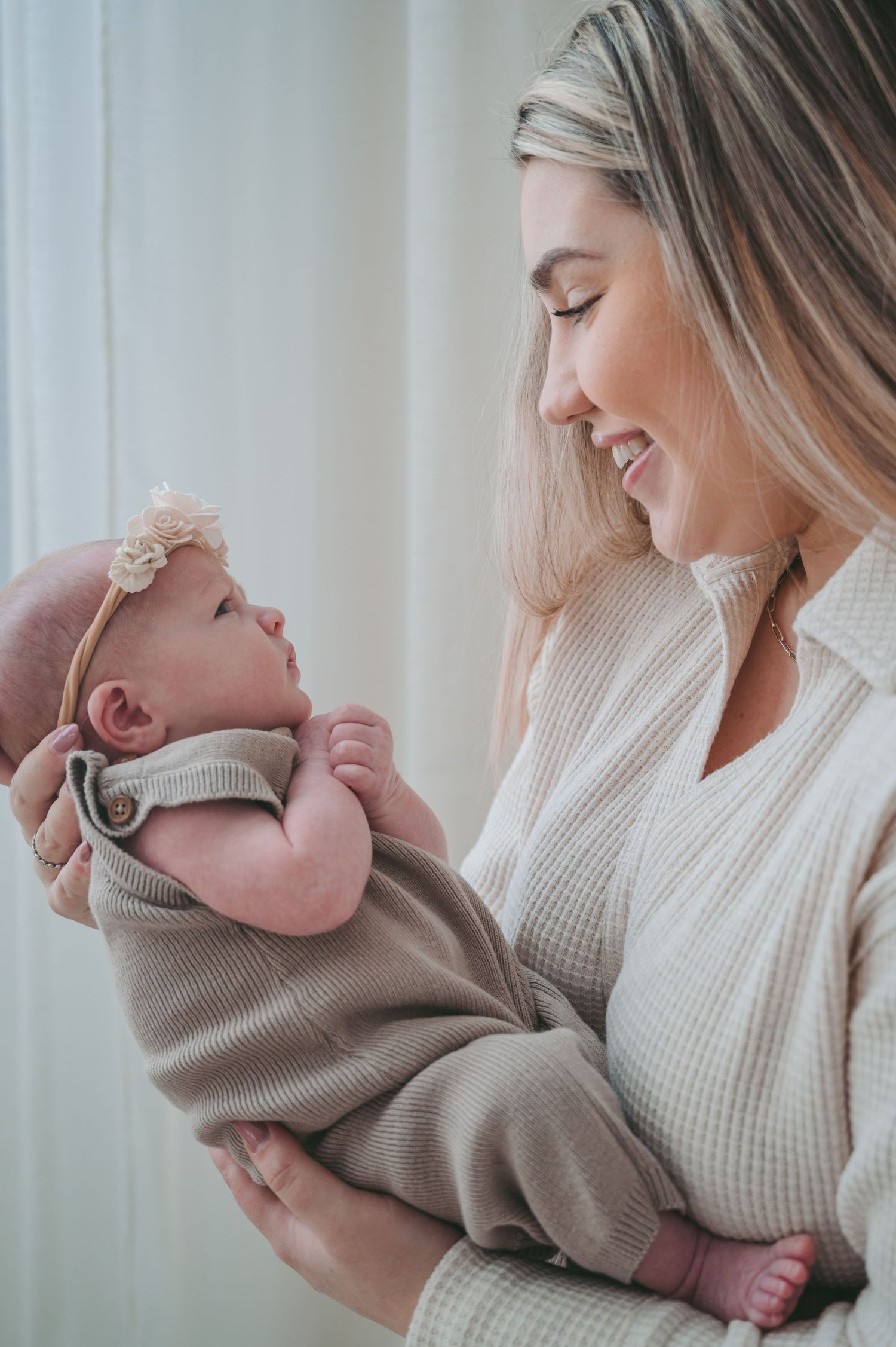 An intimate bonding moment with baby in beige outfit and floral headband being held against cream sweater.