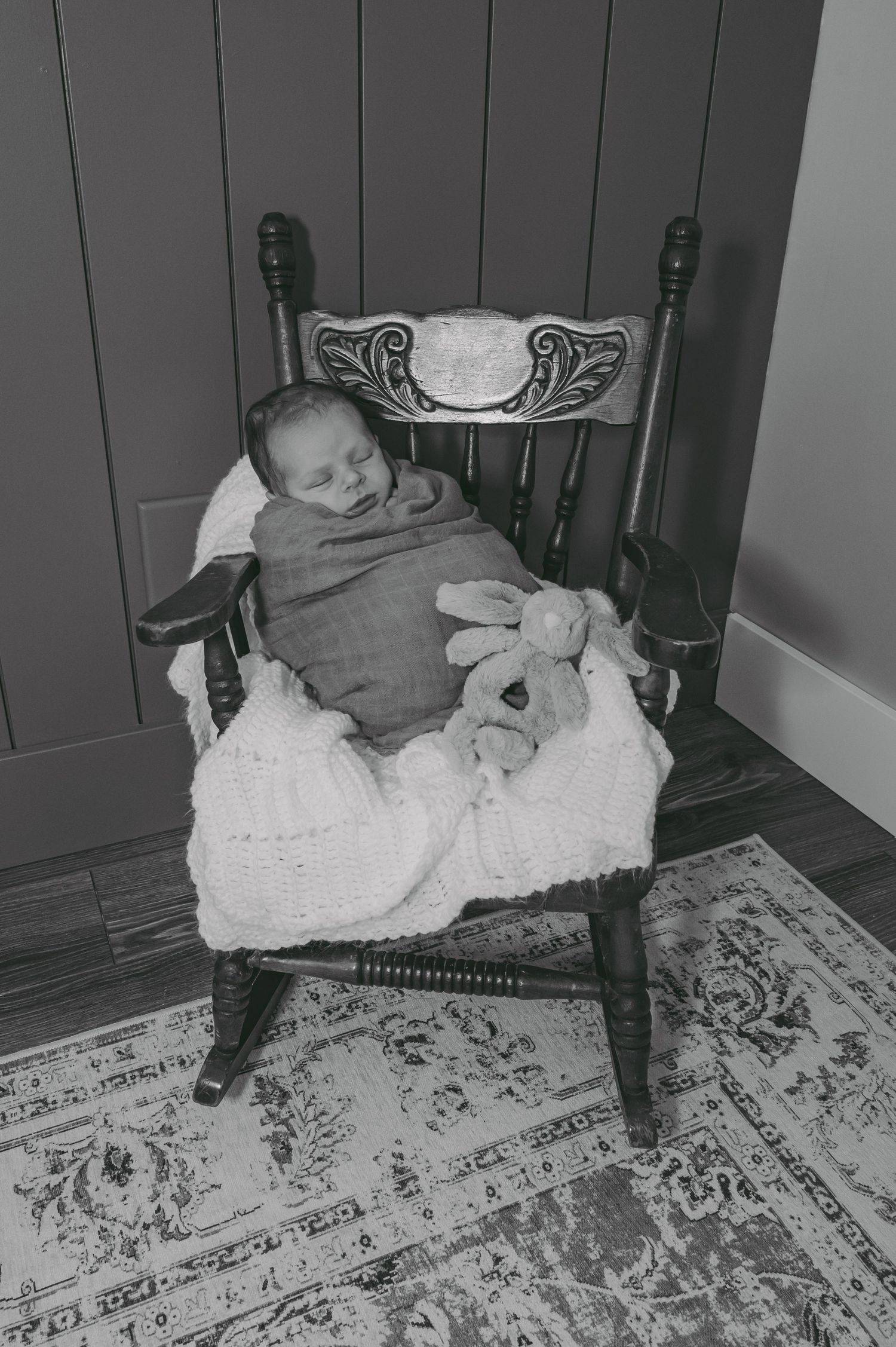 Vintage black and white photo of sleeping newborn in antique rocking chair with stuffed bunny.