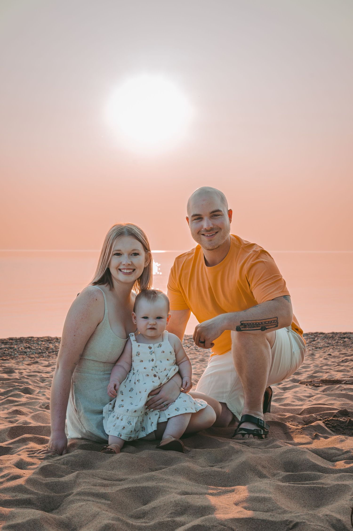 Family sitting together on a sandy beach at sunset with warm golden lighting.