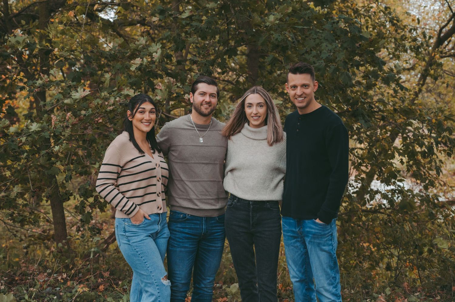 A group stands together in casual attire against an autumn backdrop with golden foliage.